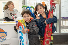 Two children holding a large tube of toothpaste and toothbrush.